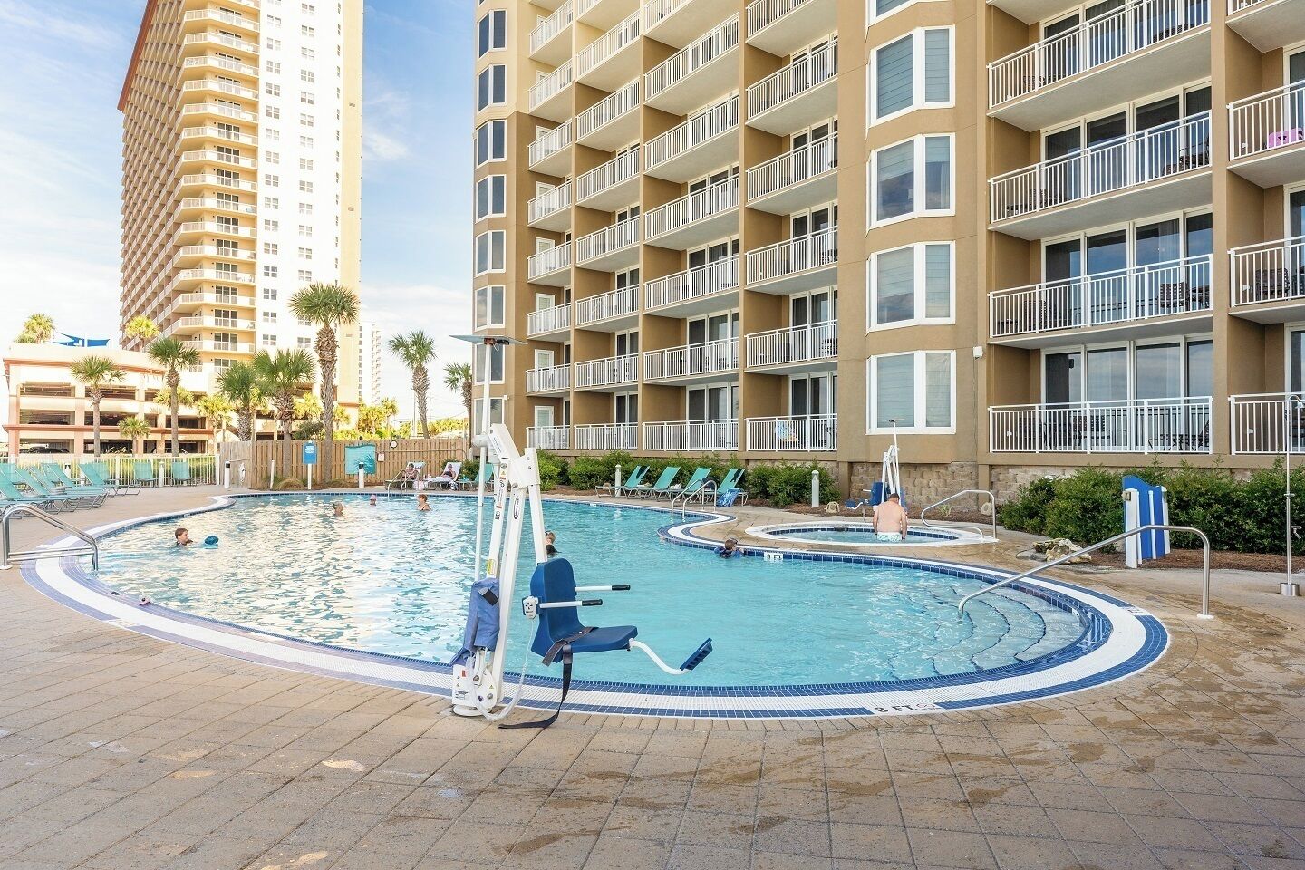Un hotel con piscina, varios balcones y un edificio alto al fondo.