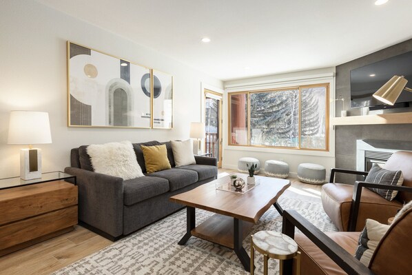A modern living room with a grey sofa, a wooden coffee table, and a large window with a snowy view. - Managed by Park City Lodging-True Ski-In/Ski-Out to Park City Mountain Resort! (Park City)