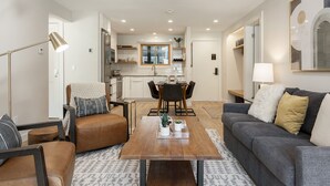 A modern living room with a sofa, coffee table, and a dining area with chairs and a table.