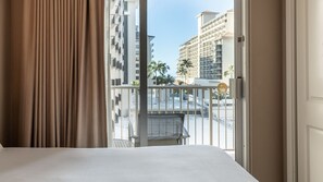 Ein Hotelzimmer mit Balkon, Bett und Blick auf hohe Gebäude.