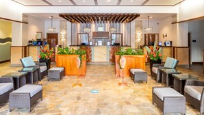 Un área de recepción con un mostrador de madera, dos zonas de estar con muebles de mimbre y un suelo de baldosas de piedra.