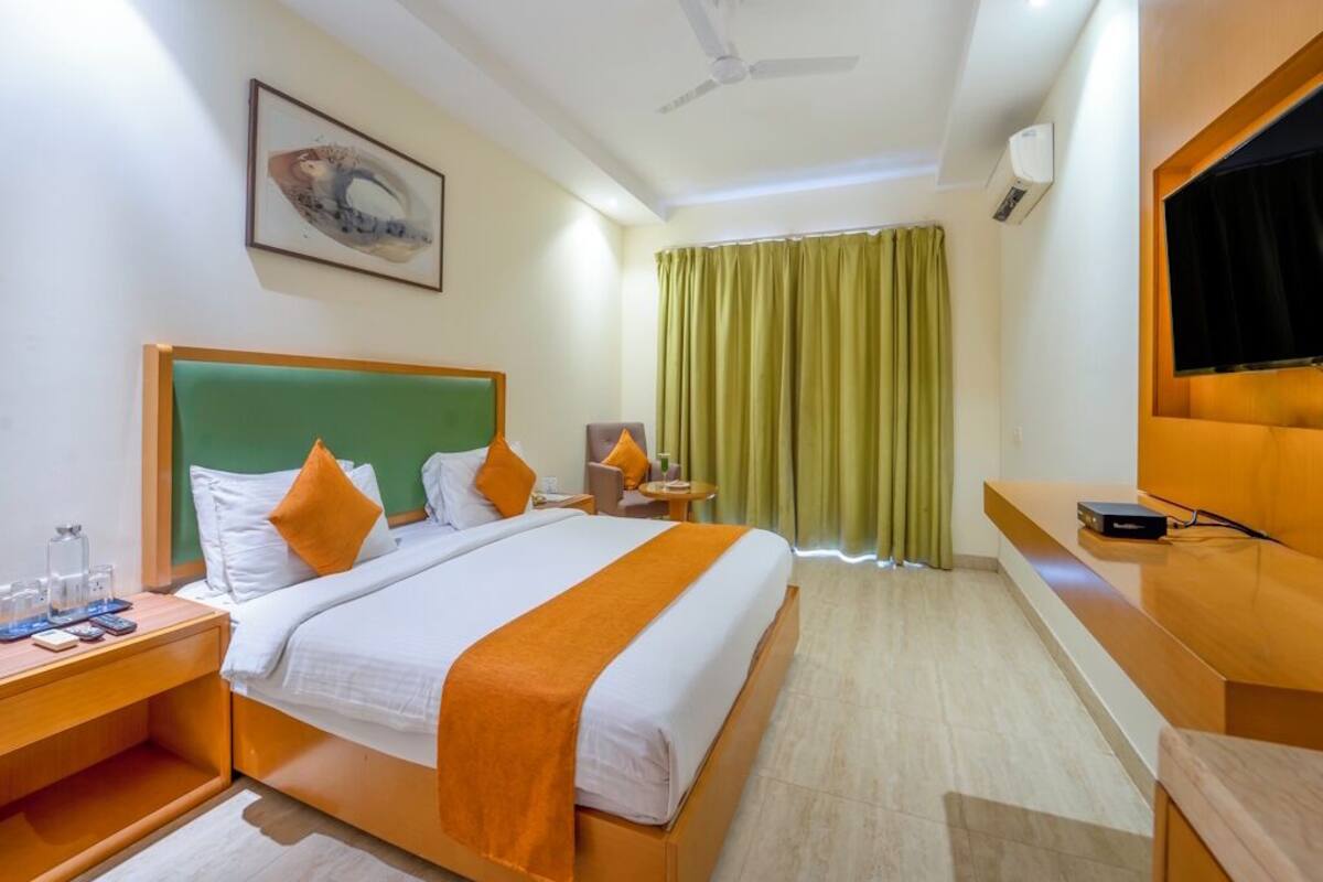 Quarto de hotel com cama, escrivaninha, cadeira, televisão e ventilador de teto.