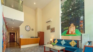 Un vestíbulo de hotel con mostrador de recepción, un sofá, una mesa de centro y un mural en la pared.