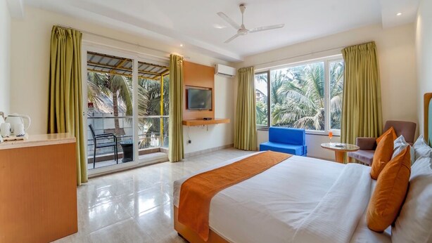 Habitación de hotel con cama, escritorio, televisor y balcón con vista a palmeras.