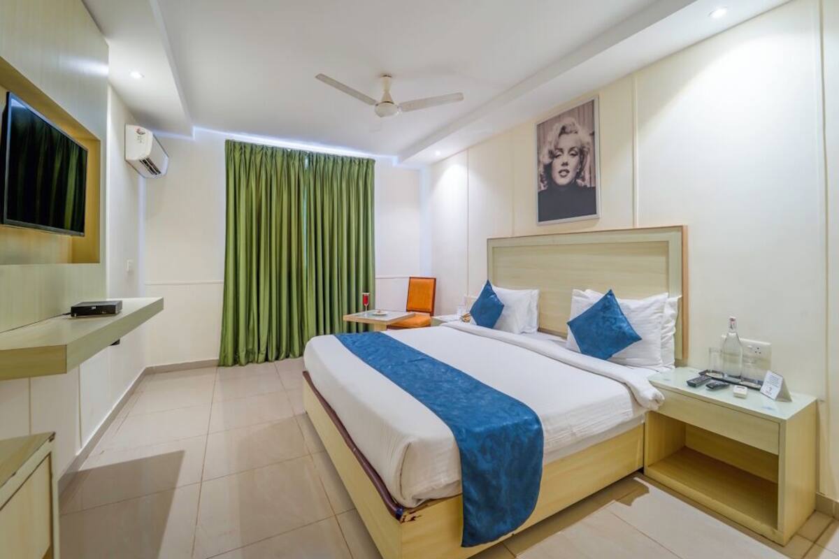 Quarto de hotel com cama, mesa de cabeceira, televisão, ar condicionado e ventoinha de teto.