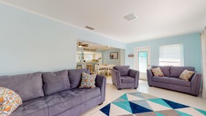 A living room with two grey sofas, a patterned rug, and a kitchen visible in the background. - Tropical Oasis - Englewood Beach, FL. (Englewood)