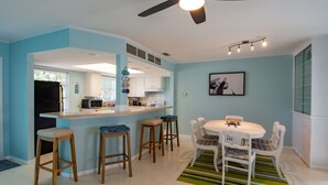 A modern kitchen with a bar area, white bar stools, and a dining table with chairs. - Tropical Oasis - Englewood Beach, FL. (Englewood)