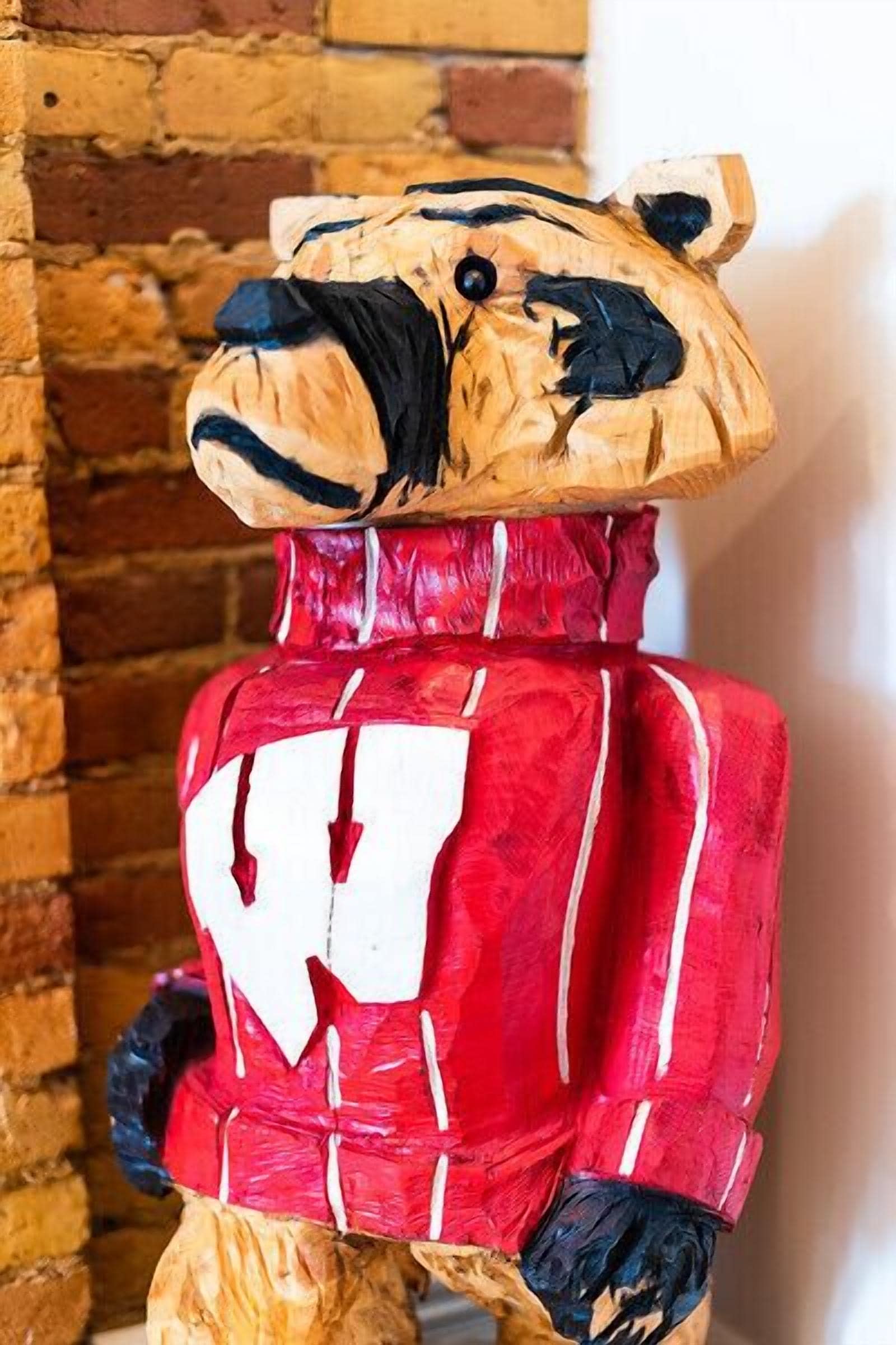 A wooden sculpture of a bear wearing a red jacket with white stripes.