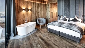 A modern bedroom with a large bed, a built-in bathtub, and wooden paneling. - Ski-in ski-out chalet with sauna (Kaltenbach)