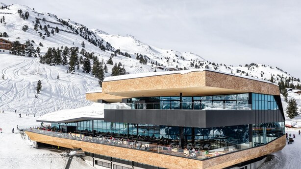 A modern ski resort building with a glass facade, ski slopes in the background, and a mountainous landscape. - Ski-in ski-out chalet with sauna (Kaltenbach)