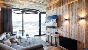 A modern living room with a large TV, wooden wall paneling, a sofa, and a fireplace. - Ski-in ski-out chalet with sauna (Kaltenbach)