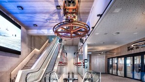 A modern indoor space with two escalators, a large digital screen, and a ceiling with industrial lighting fixtures. - Ski-in ski-out chalet with sauna (Kaltenbach)