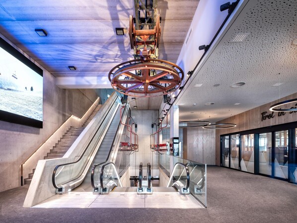 Un intérieur moderne avec des escaliers mécaniques, un grand écran numérique et un mur en bois orné de panneaux indicateurs.