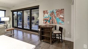 A modern living room with a dining area, large glass sliding doors leading to a balcony, and a colorful abstract painting on the wall. - Biltmore Avenue Balcony Condo (Asheville)