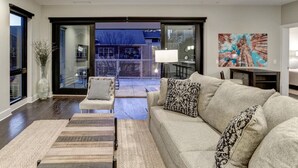 A modern living room with a large sofa, a coffee table, and a view of a balcony. - Biltmore Avenue Balcony Condo (Asheville)