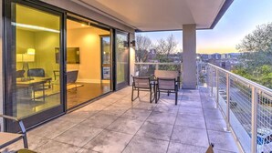 A balcony with a glass door leading to a room, a table with chairs, and a view of the cityscape. - Biltmore Avenue Balcony Condo (Asheville)