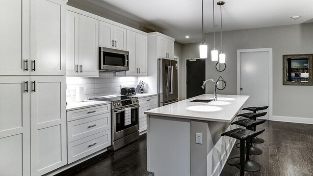A modern kitchen with white cabinets, stainless steel appliances, a central island with bar stools, and pendant lighting. - Biltmore Avenue Balcony Condo (Asheville)