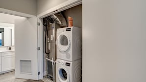 A laundry room with stacked washers and dryers, a vent, and a door leading to a bathroom.