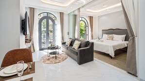 A modern hotel room with a sofa, a dining table set, a bed, and large windows with curtains.