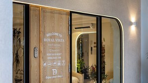 A hotel entrance with a wooden door displaying the name 'ROYAL VISTA' and amenities like 24/7 support, phone numbers, and payment options.