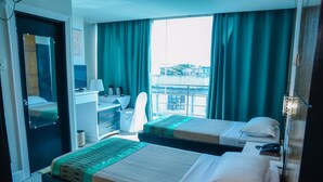 A hotel room with two beds, a desk, a chair, and a large window with curtains. - Marcian Business Hotel (Zamboanga)