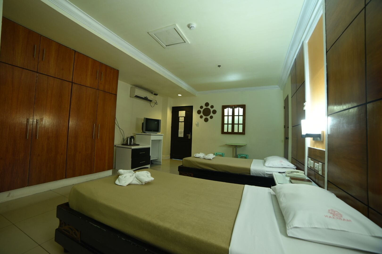 Habitación de hotel con dos camas, un escritorio con computadora, un televisor y un armario.