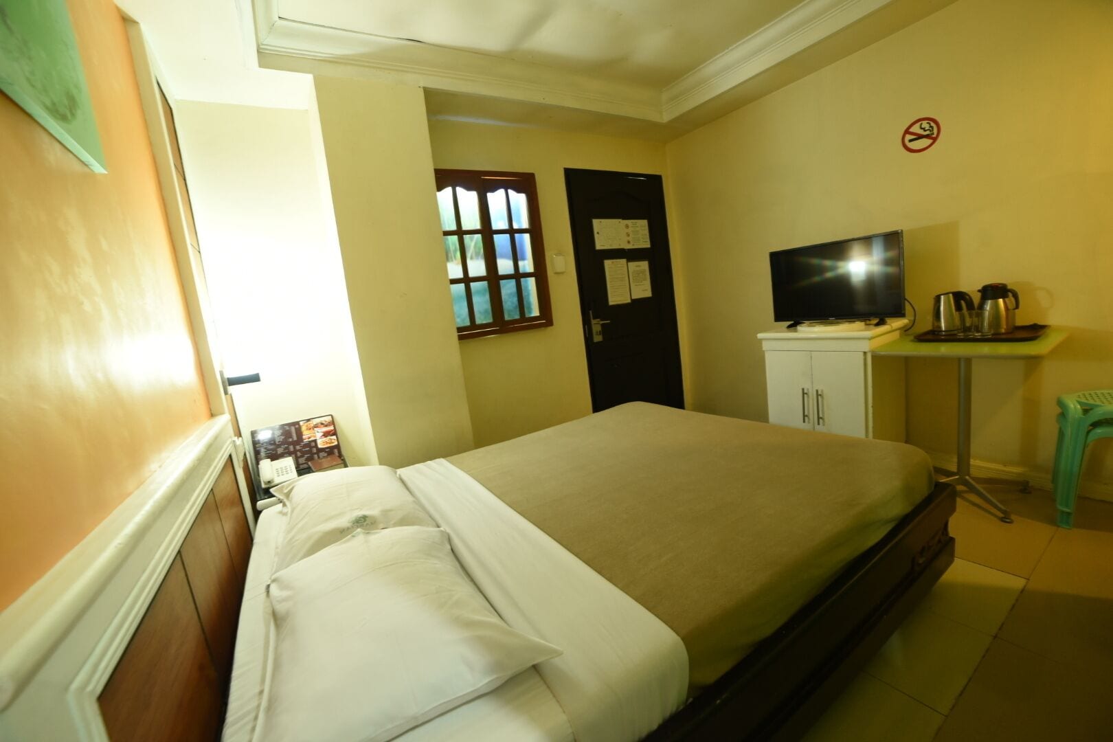 A hotel room with a bed, a desk with a television, a coffee maker, and a door with a window.
