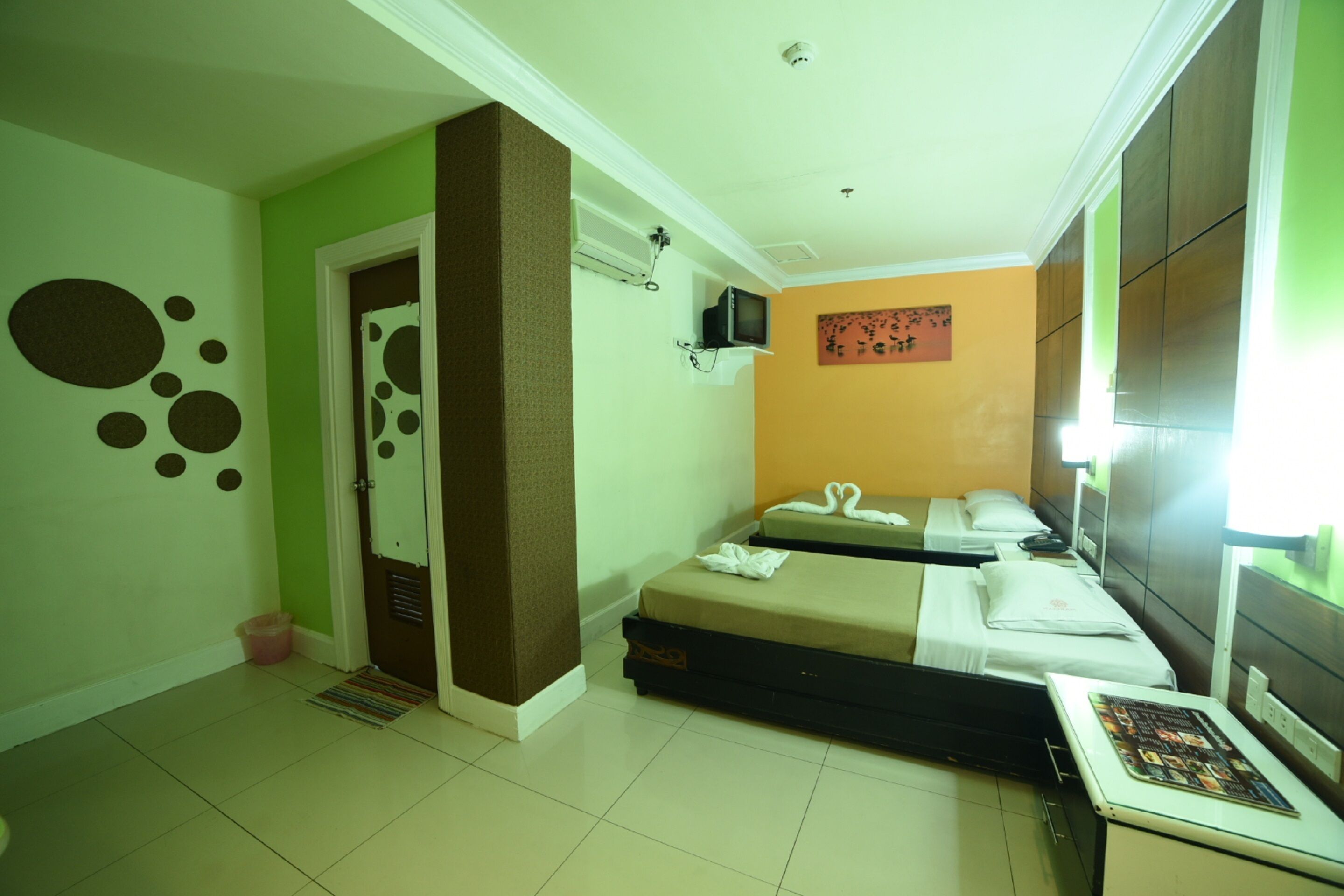 A hotel room with two beds, a television on the wall, and a small table with a magazine.