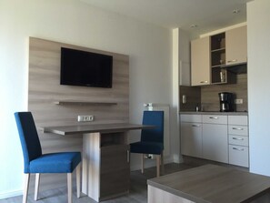 Une cuisine moderne équipée d’un téléviseur encastré, d’une table à manger avec des chaises et d’une machine à café.