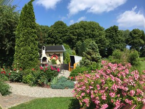Un jardin agrémenté d’un petit bâtiment doté d’une cheminée, entouré d’une végétation luxuriante et de plantes en fleurs.