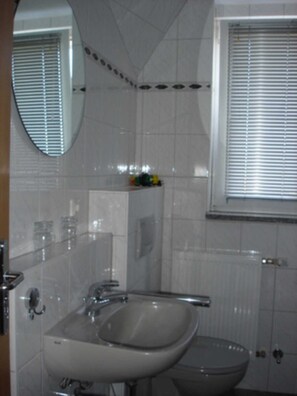 A bathroom with a white sink, a toilet, a mirror, and a window with blinds. - App. 602 - Apartment complex Zur Seemöwe (Ostseebad Insel Poel)