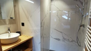Une salle de bain moderne avec un meuble-lavabo en marbre, un évier, un miroir et une douche séparée par des parois en verre.