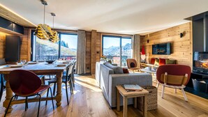 Un espace de vie et de salle à manger moderne, à aire ouverte, avec un plancher en bois, un canapé, une table à manger et des chaises. De grandes fenêtres offrent une vue sur l’extérieur.