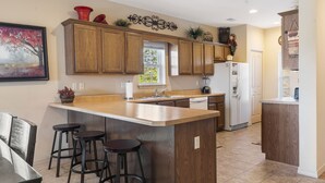 A modern kitchen with wooden cabinets, a central island with stools, a refrigerator, and a window with a view of greenery. - Walk-In 3 BD/3BA Condo -Covered Deck with Pool View, Golf/Ticket Discounts, Resort Perks (Branson)