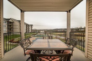 Varanda coberta com mesa e cadeiras, dando vista para uma área residencial com casas e um parque.