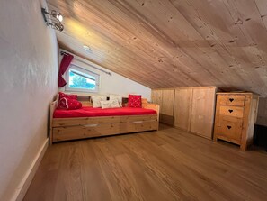 A cozy attic bedroom with a wooden bunk bed, a window with a view, and a wardrobe with heart-shaped handles. - Bright apartment, near slopes, pets allowed (La Clusaz)