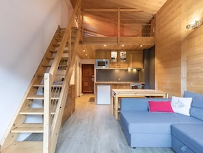 A wooden interior with a staircase, a kitchen, and a sofa.