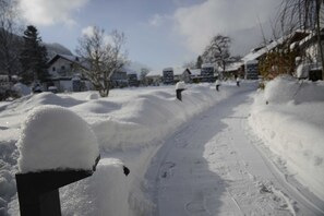 Une rue résidentielle enneigée, avec des maisons, un ciel dégagé et une boîte aux lettres recouverte de neige.