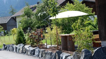 Ein Wohngebiet mit einer Steinmauer, einer hölzernen Bank und einem weißen Sonnenschirm.