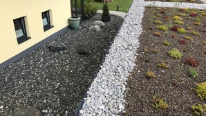 Ein Gebäude mit Flachdach, einem Kiesweg und einem kleinen Gartenbereich mit verschiedenen Pflanzen.