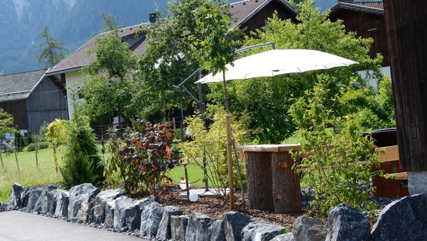Un quartier résidentiel avec un mur en pierre, un banc en bois et un parasol blanc.