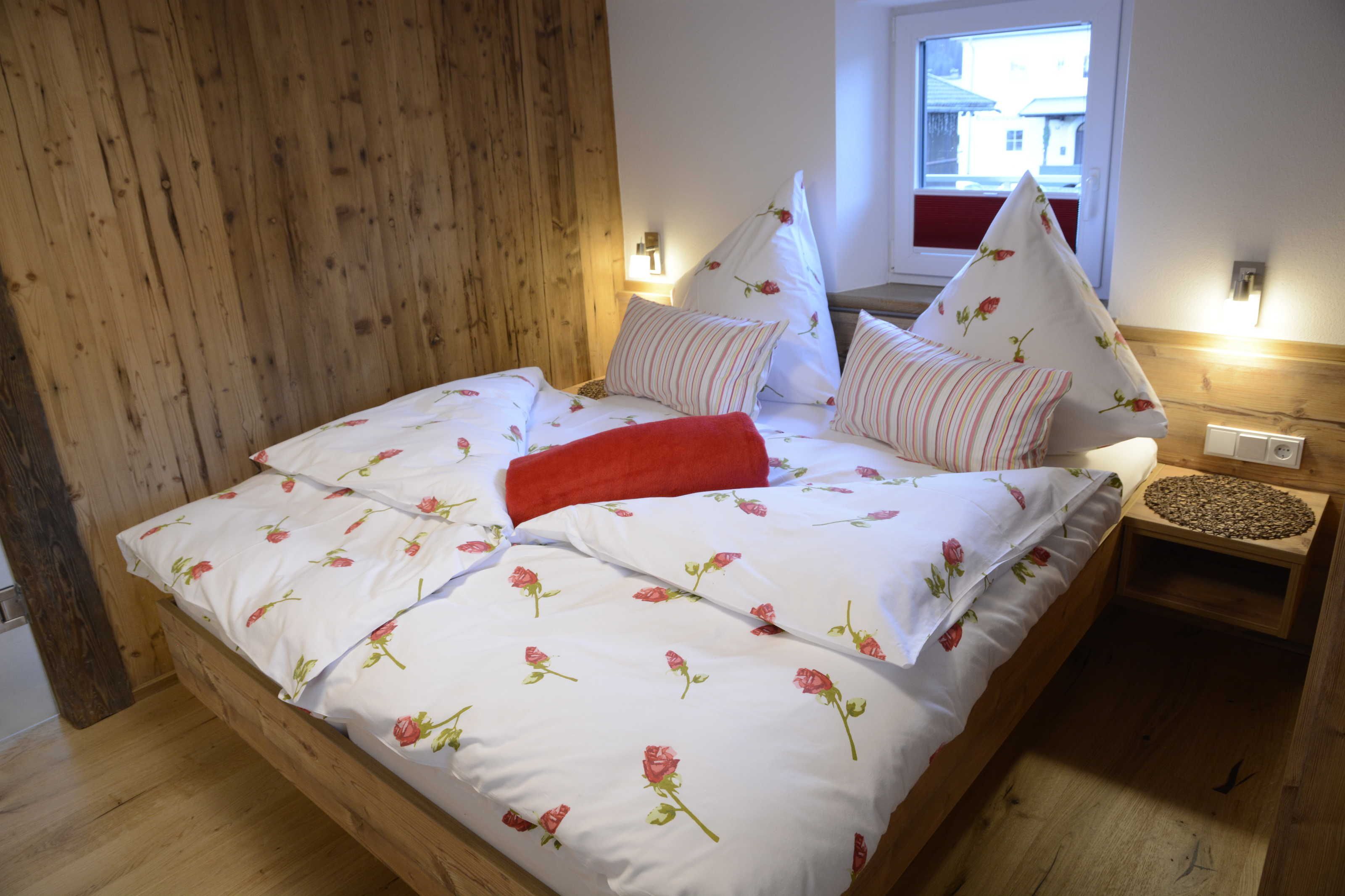 Ein hölzernes Bett mit floralem Bettzeug, einer roten Decke und einem Nachttisch mit Lampe.