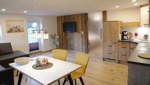 A modern kitchen with wooden cabinets, a built-in oven, and a flat-screen TV. - Thanellerapart - Alpenapart Singer (Ehenbichl)