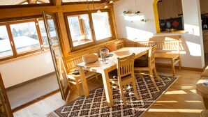 Et spiseområde i træ med et bord og stole, store vinduer og udsigt ud.