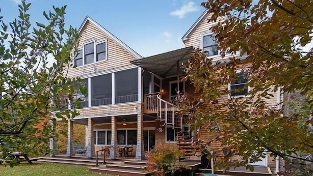 A two-story house with a covered porch, a staircase leading to the upper floor, and a small outdoor seating area. - 1/4 Acre Woods on Lake Waukewan! (Meredith)