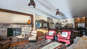 A cozy living room with a stone fireplace, leather armchairs, a coffee table, and a dining area with wooden cabinets and a staircase. - 1/4 Acre Woods on Lake Waukewan! (Meredith)