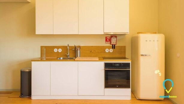 A compact kitchen with white cabinets, a stainless steel sink, a built-in oven, and a white refrigerator. - HISTORY PORTO - Classy Duplex Apartment in the historic center (Porto)
