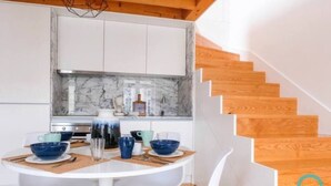 Une cuisine moderne avec des meubles blancs, un pare-feu en marbre et un coin repas comprenant une table et des chaises blanches.