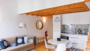 Un salon moderne comprenant un canapé, une table de salle à manger ronde avec des chaises, un coin cuisine avec des meubles blancs et un plafond en bois.