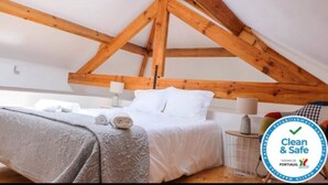 Une chambre avec une structure de plafond en bois, un lit avec une literie blanche et une serviette sur le sol.